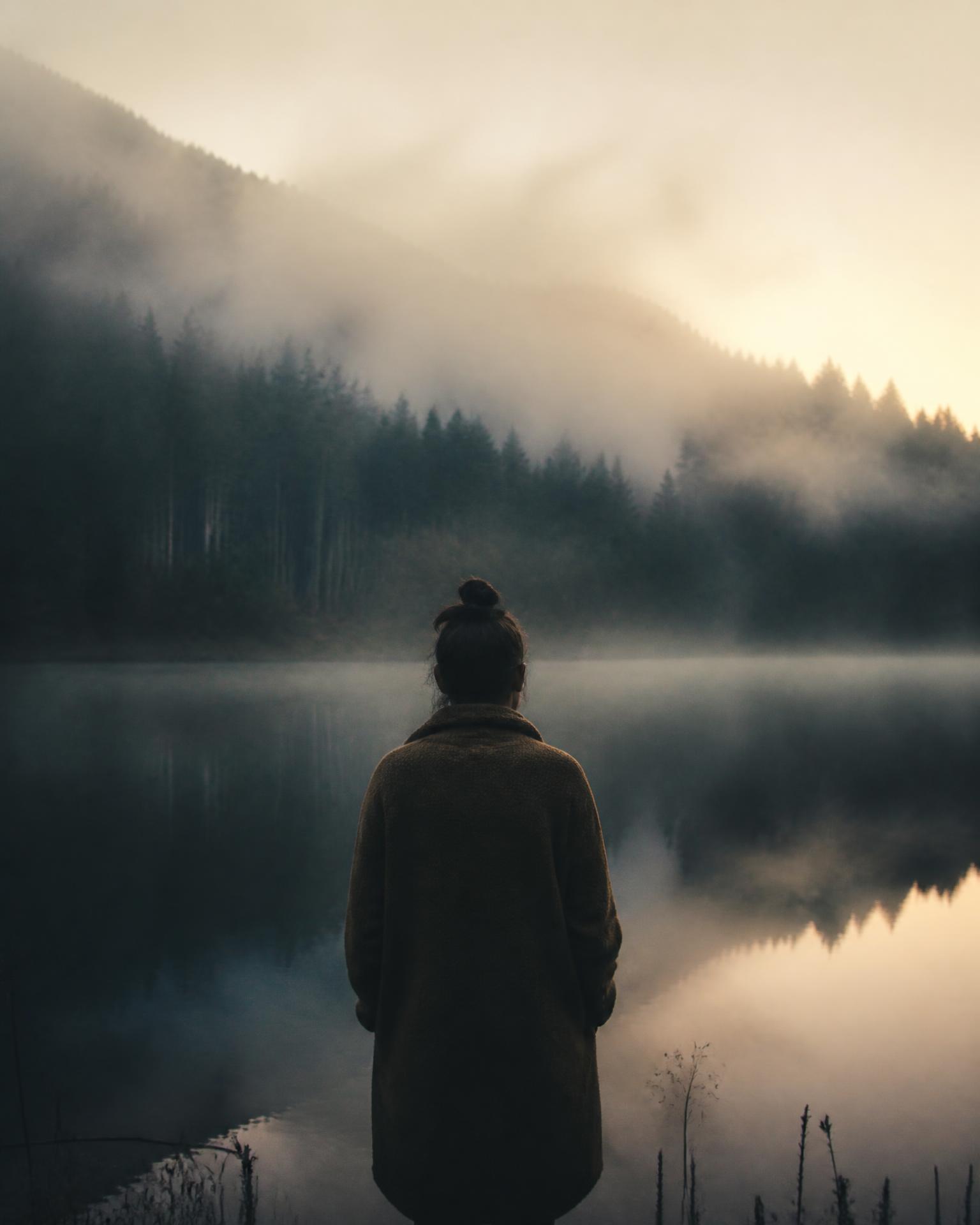 A person standing at a misty lake at first light